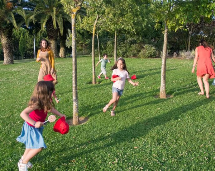 Kids and adults enjoy playing together in a lush, sunny park setting.